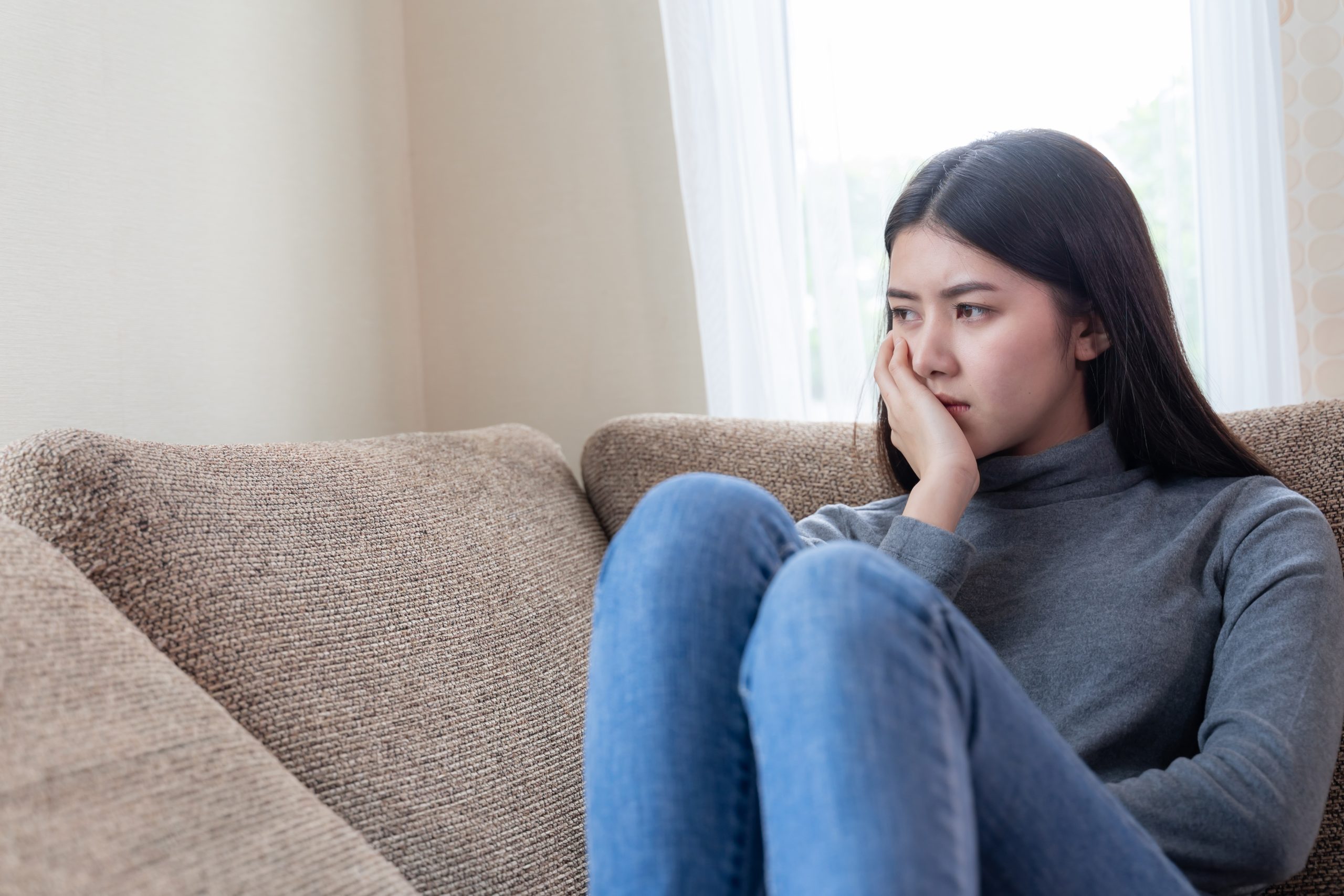 Close up face of Asian young woman siting alone on couch